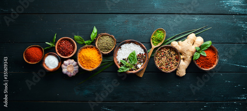 Large spice and herb collection in bowls and spoons. Indian spices. On a black wooden background. Top view.