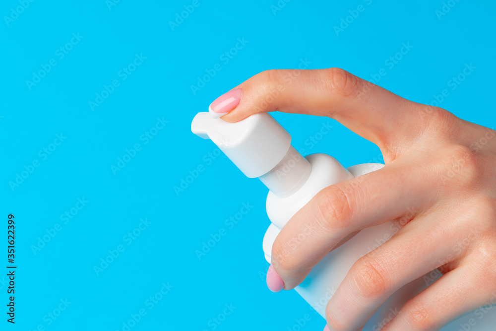 Female hand holding skincare product bottle on blue Female hand holding skincare product bottle on blue