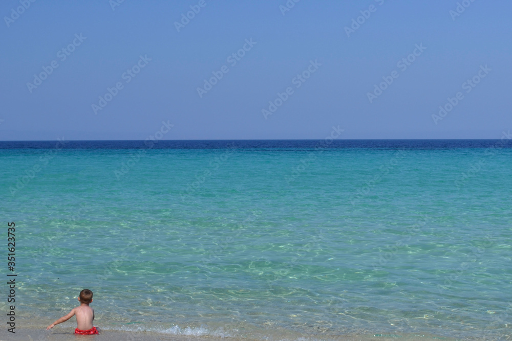 Ребенок сидит на берегу и смотрит на море