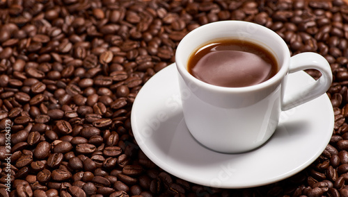 A cup of coffee  stands on coffee beans.