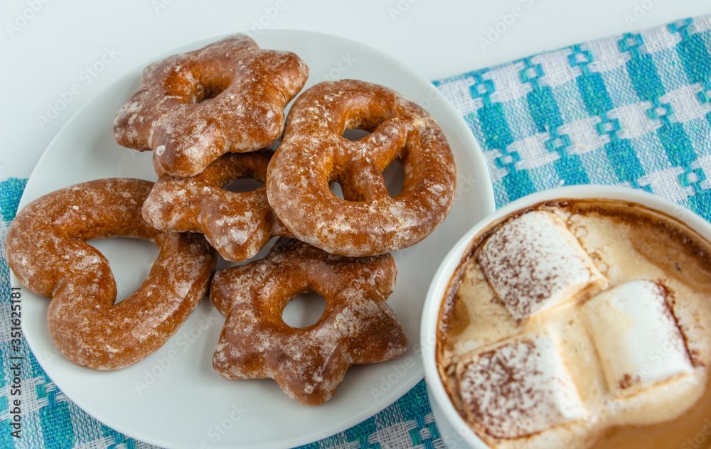 fragrant gingerbread cookies on a white plate with a cup of warm cocoa or coffee with marshmallow, sprinkled with chocolate, white background, blue napkin, delicious dessert, feeling of comfort fragrant gingerbread cookies on a white plate with a cup of warm cocoa or coffee with marshmallow, sprinkled with chocolate, white background, blue napkin, delicious dessert, feeling of comfort