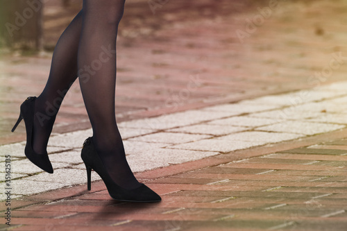 Close up of woman legs in black stockings wearing black high heels on the street.