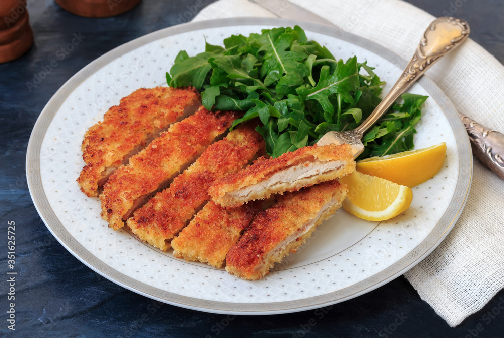 Pan fried chopped pork schnitzel with arugula and lemon on dark background close up Pan fried chopped pork schnitzel with arugula and lemon on dark background close up