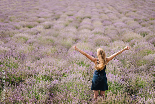 Fototapeta Naklejka Na Ścianę i Meble -  Beautiful girl in dress stand on purple the lavender field. Beautiful woman walk and look on the lavender field on sunset in France. Soft focus. Enjoy on the floral glade, summer nature. Back view.
