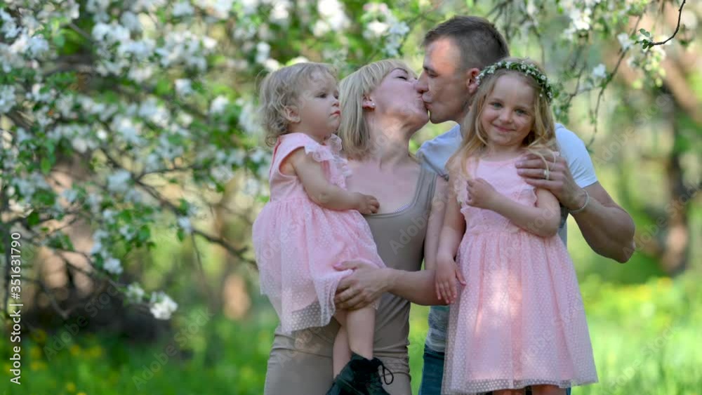 Portrait of a happy family in a flowered park. Beautiful family plays against the backdrop of a blossoming apple tree. Kissing and hugging happy family. family childhood concept Portrait of a happy family in a flowered park. Beautiful family plays against the backdrop of a blossoming apple tree. Kissing and hugging happy family. family childhood concept