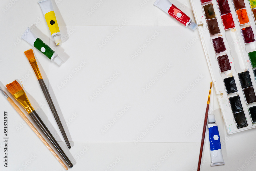 White paper sheet and painting brushes and paints on the table White paper sheet and painting brushes and paints on the table
