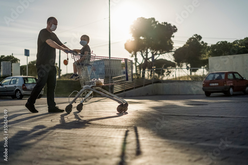 Father pushing shopping cart with his little son. Both wearing protective masks.