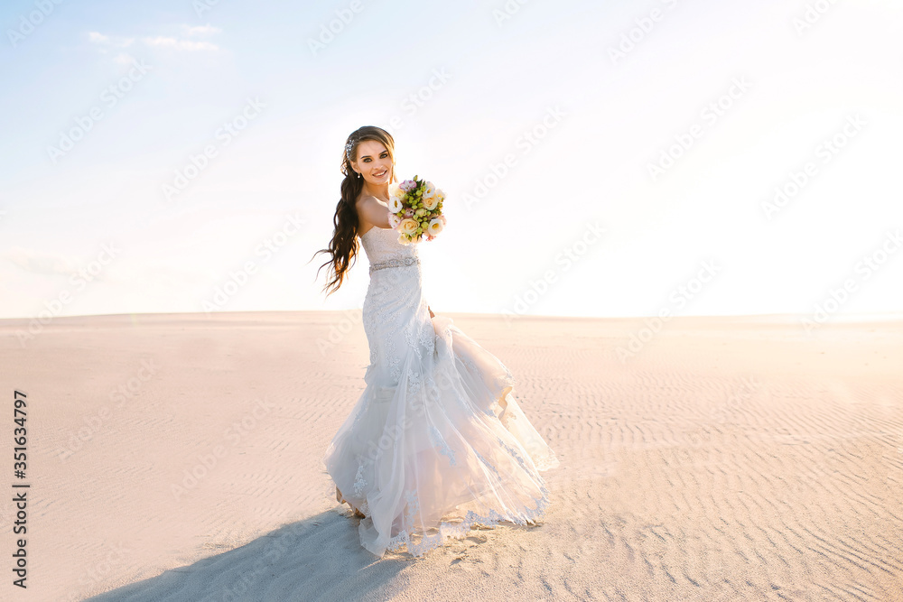 beautiful smiling bride in a white wedding dress walks in the sandy desert, a brunette girl with a wedding bouquet is spinning and having fun, sunset beautiful smiling bride in a white wedding dress walks in the sandy desert, a brunette girl with a wedding bouquet is spinning and having fun, sunset