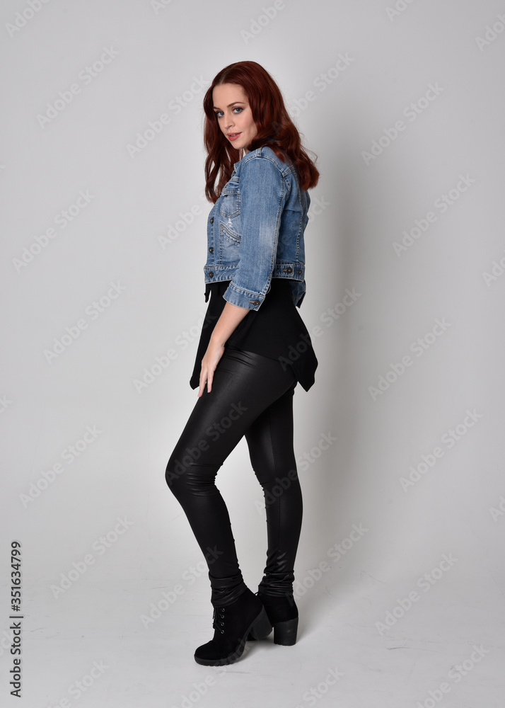 portrait of a pretty girl with red hair wearing black leather pants and denim  jacket. Full length standing pose in side profile isolated against a grey  studio background Stock Photo | Adobe