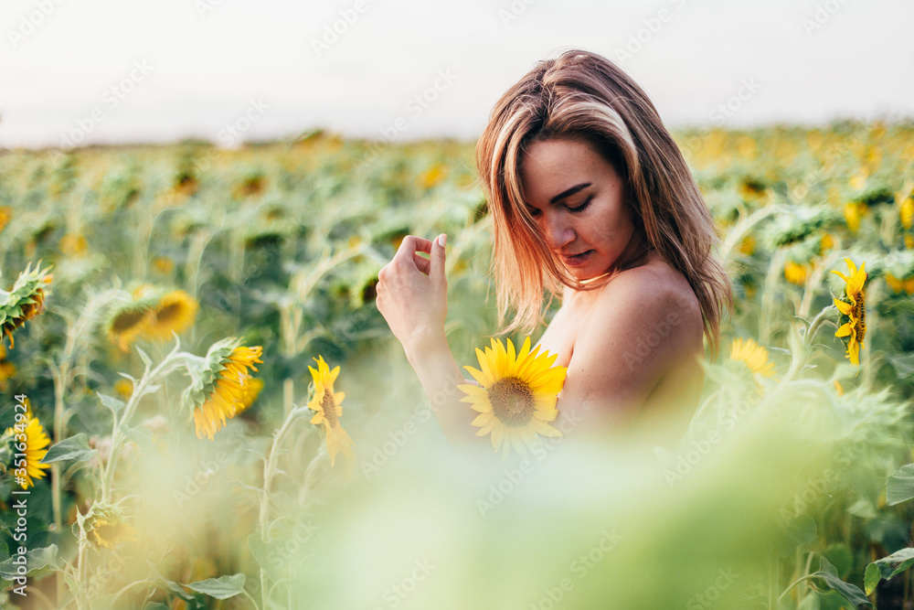 A young topless girl stands in sunflowers