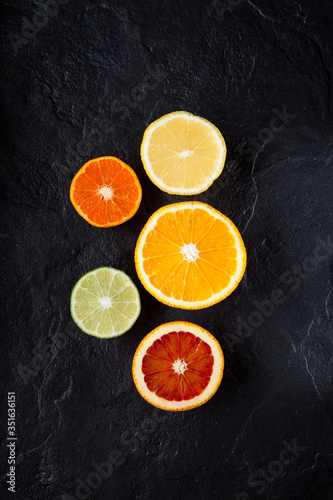 Sliced fresh ripe citruses. Lemon, lime, red orange and mandarin on a dark stone background. Top view with copy space © AB-7272