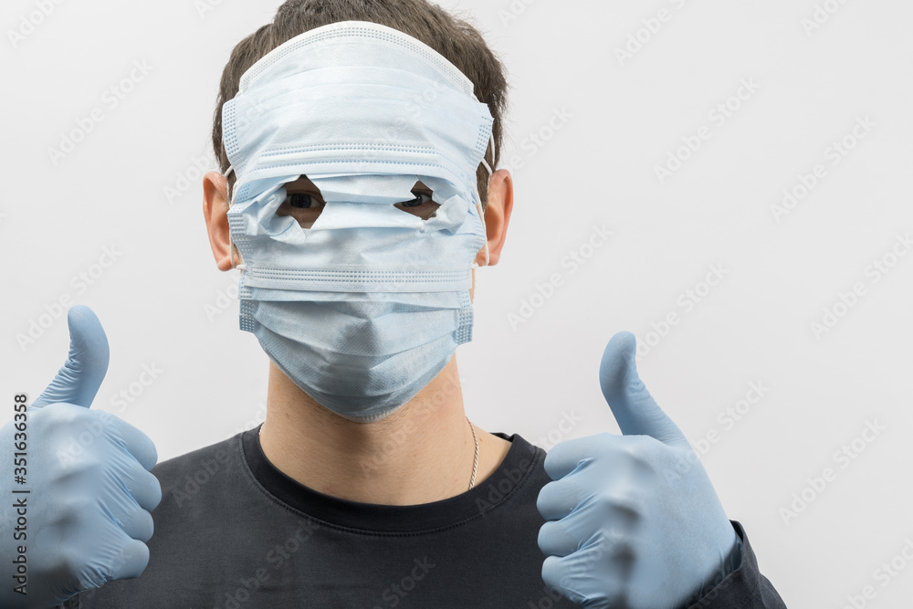 Young european man wearing mask against the corona virus and thumbs up covid 19 man wearing reusable surgical mask to prevent from virus white\grey background Corona virus pandemic funny fun