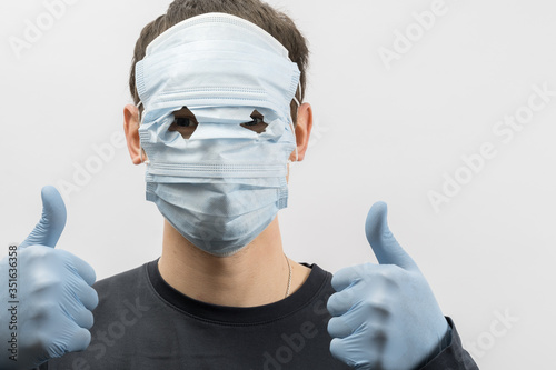 Young european man wearing mask against the corona virus and thumbs up covid 19 man wearing reusable surgical mask to prevent from virus white\grey background Corona virus pandemic funny fun