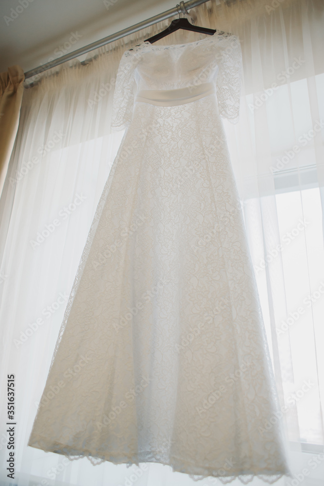 Wedding lace dress of the bride weighs on a wooden hanger. Cream cream dress. The morning of the bride. Visiting ceremony. Bride and groom. Wedding. Сocktail dress, evening dress.