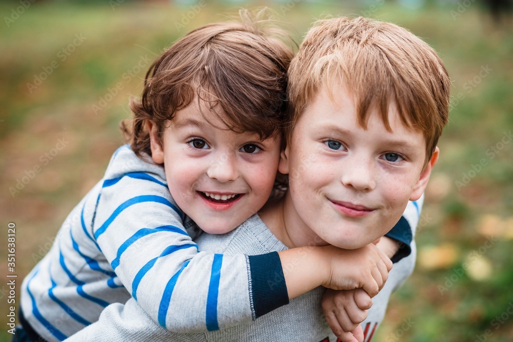 Two happy boys, happy brothers who are smiling happily together. Brothers  play outdoors in summer, best friends. Little brother with brother on his  back. Two brothers in the woods. Fraternal relations Stock