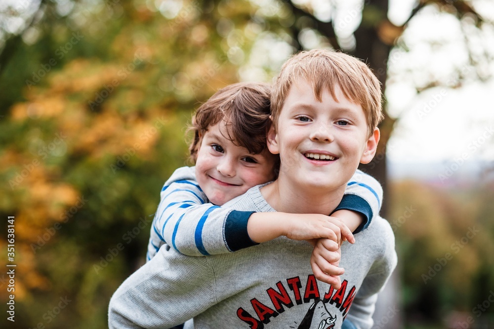 Two happy boys, happy brothers who are smiling happily together. Brothers play outdoors in summer, best friends. Little brother with brother on his back. Two brothers in the woods. Fraternal relations