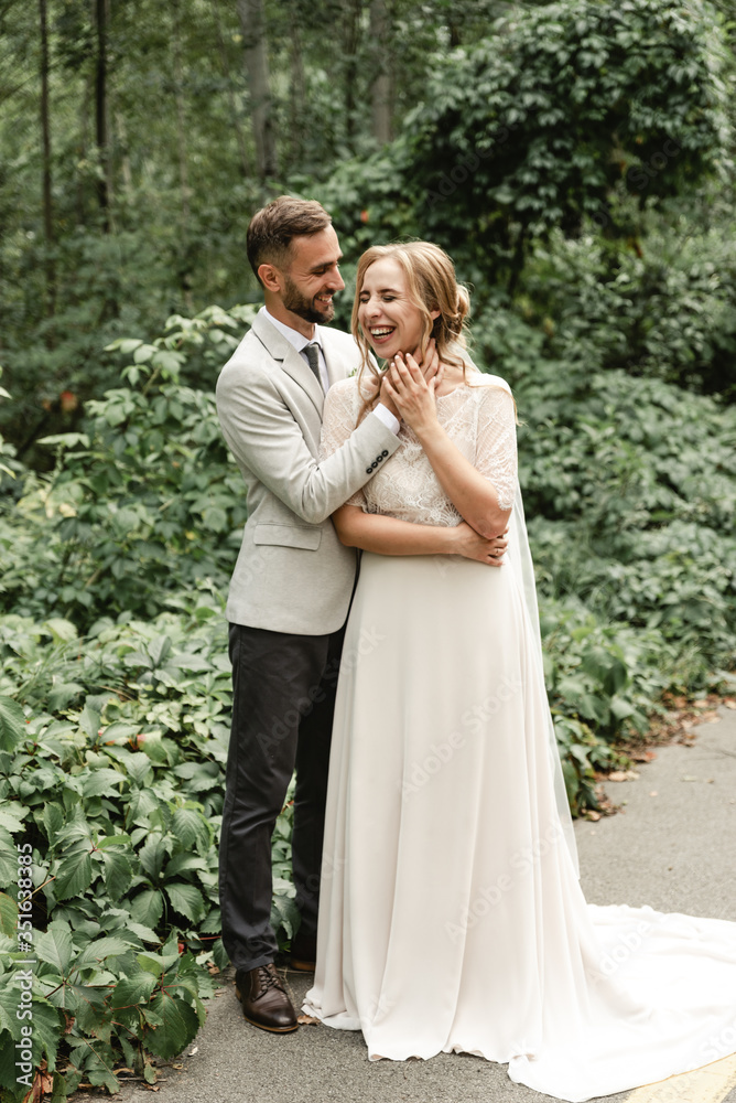 holiday newlyweds,tender hugs of a young couple,the groom touches the face of the bride,cheerful and joyful wedding couple walks in the park holiday newlyweds,tender hugs of a young couple,the groom touches the face of the bride,cheerful and joyful wedding couple walks in the park