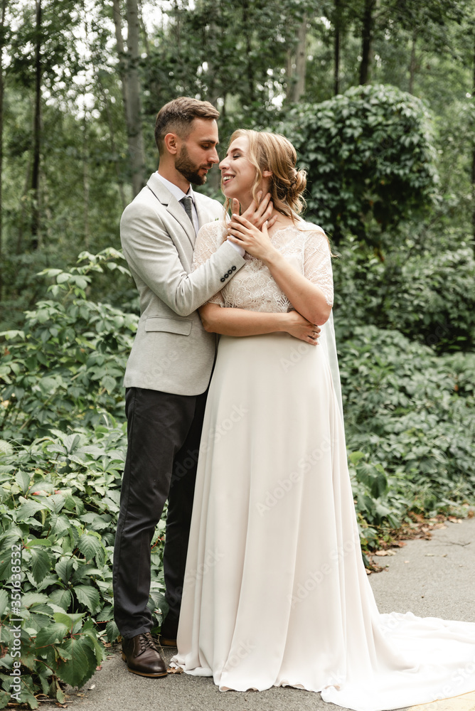 portrait of a happy wedding couple on their wedding day,beautifully dressed newlyweds tenderly hug while walking in a park,handsome bearded groom gently hugs his bride