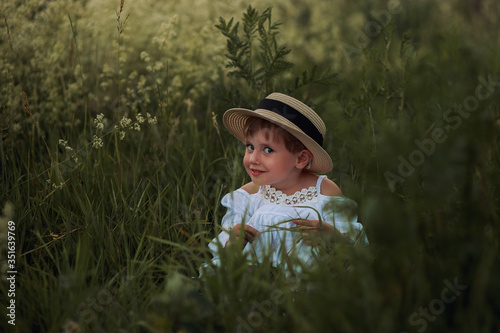  Cute little girl in a white dress and hat in the field at sunset time