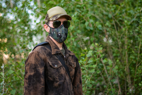 A man wearing respirator mask in sun glasses and a cap walking in the forest at COVID-19 period.