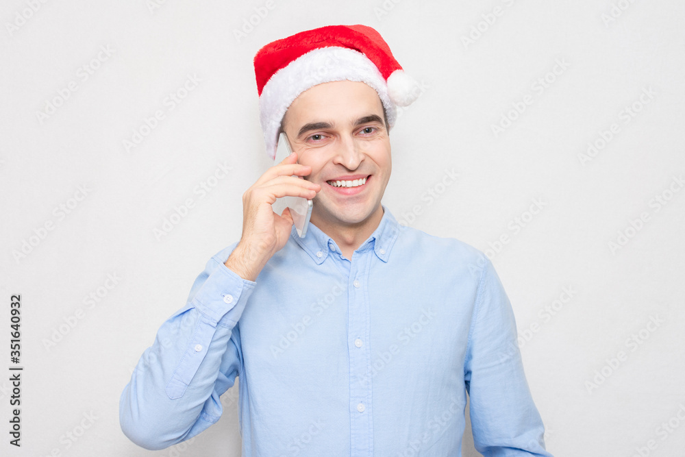 Concept of a new year. Smiling man in Santa hat talking on the phone, portrait, white background Concept of a new year. Smiling man in Santa hat talking on the phone, portrait, white background