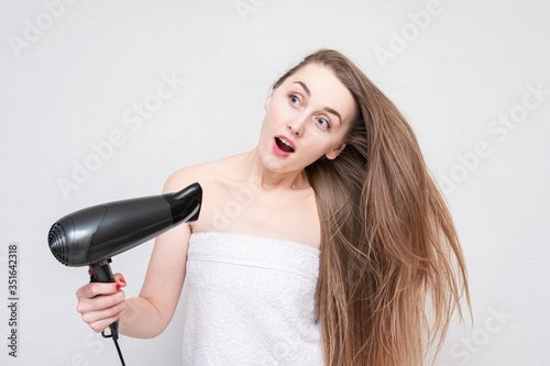 Funny girl with dryer. Portrait of an beautiful surprised young woman, white background. Hair Care