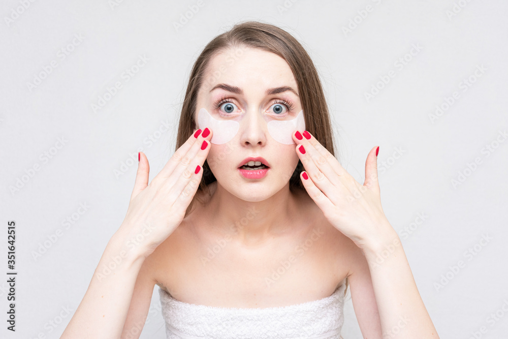 Concept of eye skin treatment. Shocked young woman using white under eye patches, white background Concept of eye skin treatment. Shocked young woman using white under eye patches, white background