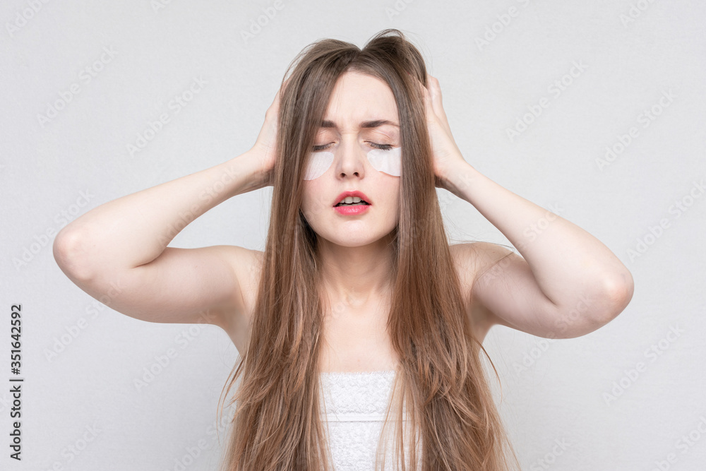 Woman with a hangover, using white under eye patches, white background. Concept of eye skin treatment. Woman with a hangover, using white under eye patches, white background. Concept of eye skin treatment.