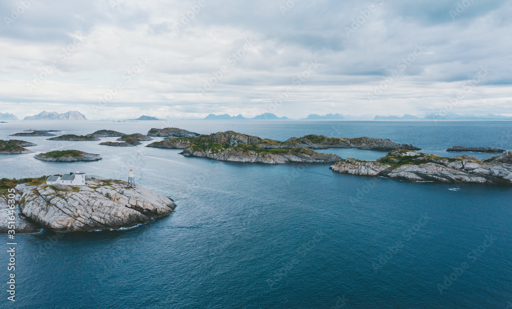 Fototapeta premium Lighthouse and island ocean aerial view in Norway Lofoten islands drone landscape stormy sky moody scenery scandinavian nature