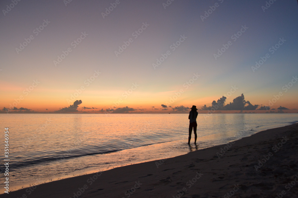 Girl in a hat walking on the beach at sunset.  Silhouette of a girl and the sea. Maldives.