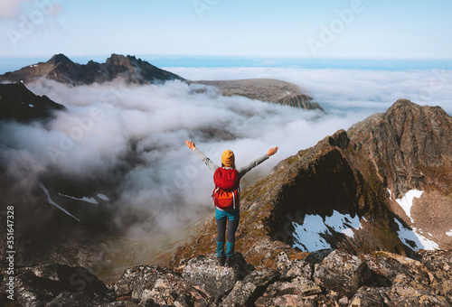 Hiker woman raised hands on mountain summit above clouds travel hiking with backpack outdoor climbing extreme adventure vacation active healthy lifestyle trekking in Norway