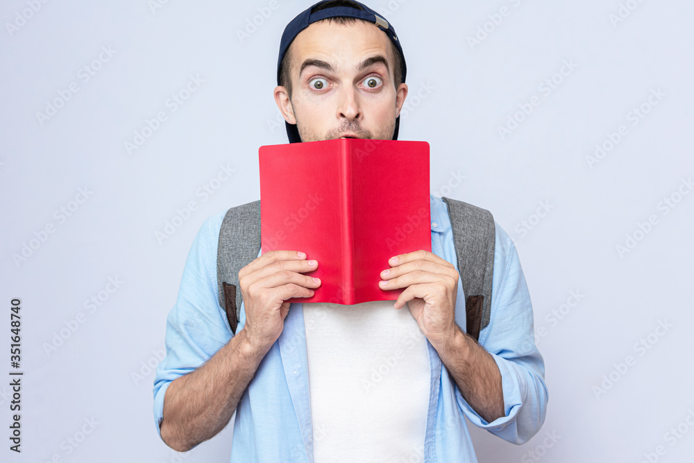 Shocked student guy with backpack reading a book, gray background, copy space