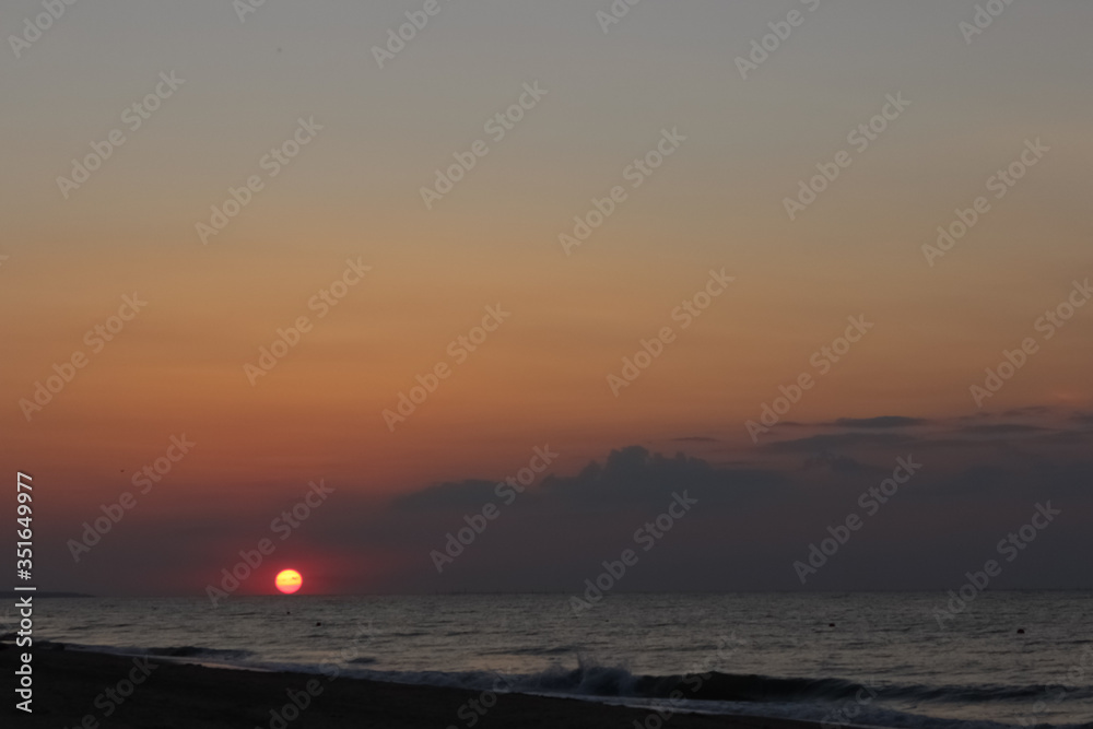  Beautiful sunset on shore of the Sea of ​​Azov. Pink sun hiding behind the horizon, orange sky and clouds