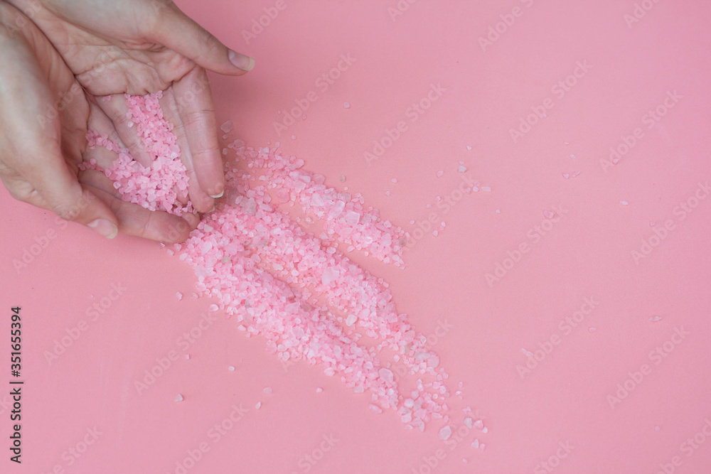 Fototapeta premium Himalayan salt on a pink background spills from the hands of a woman. Pink bath salt