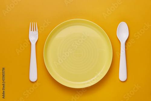 Plastic white cutlery set with yellow background. Top view