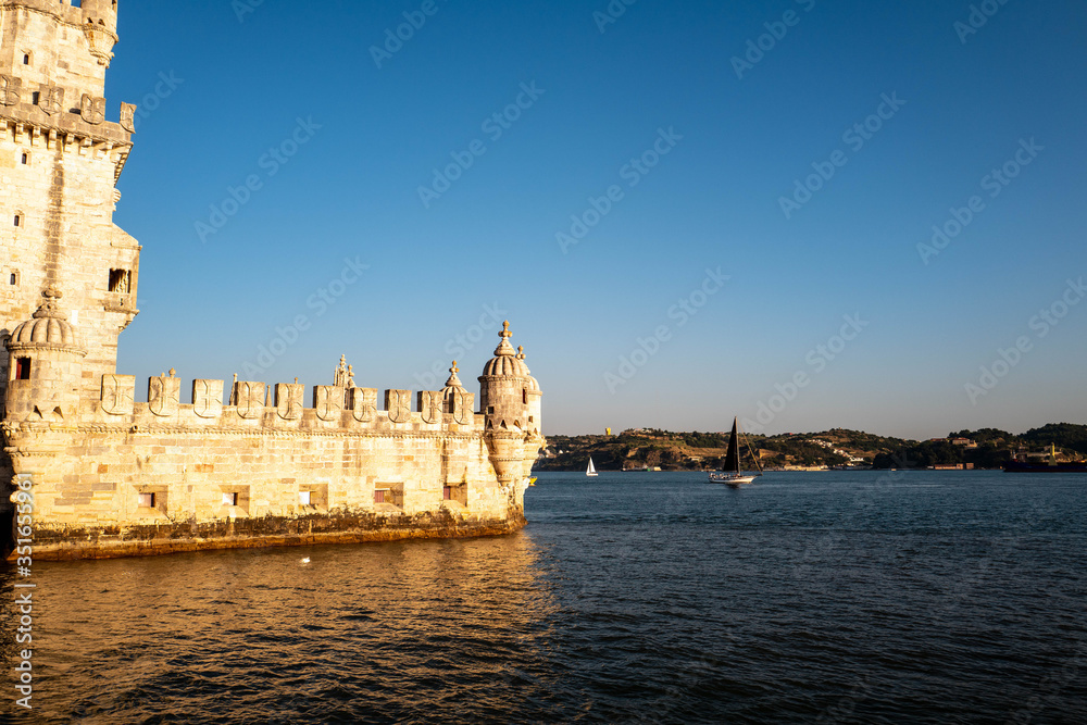 The tower of Belem in Lisbon illuminated by the setting sun with a boat passing in the background.