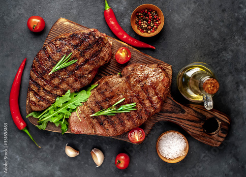 Tasty two grilled beef steaks with spices and herbs on a cutting board on a stone background