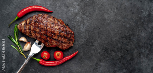 Beef steak on a meat fork with spices and herbs on a stone background with copy space for your text.