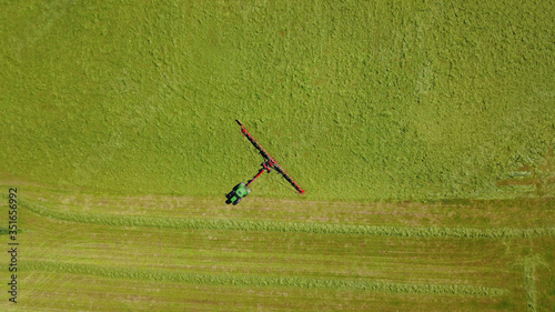 Traktor mit Heuwender bringt nach Mahd der Wiese Grasschnitt für Grassilage in Reihe, Landwirtschaft aus der Vogelperspektive photo