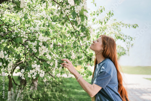 young red haired woman smelling white flowers. long ginger hair. Beautiful slim woman with very long groomed hair walking in the forest. hair care concept.  © Yulia Panova