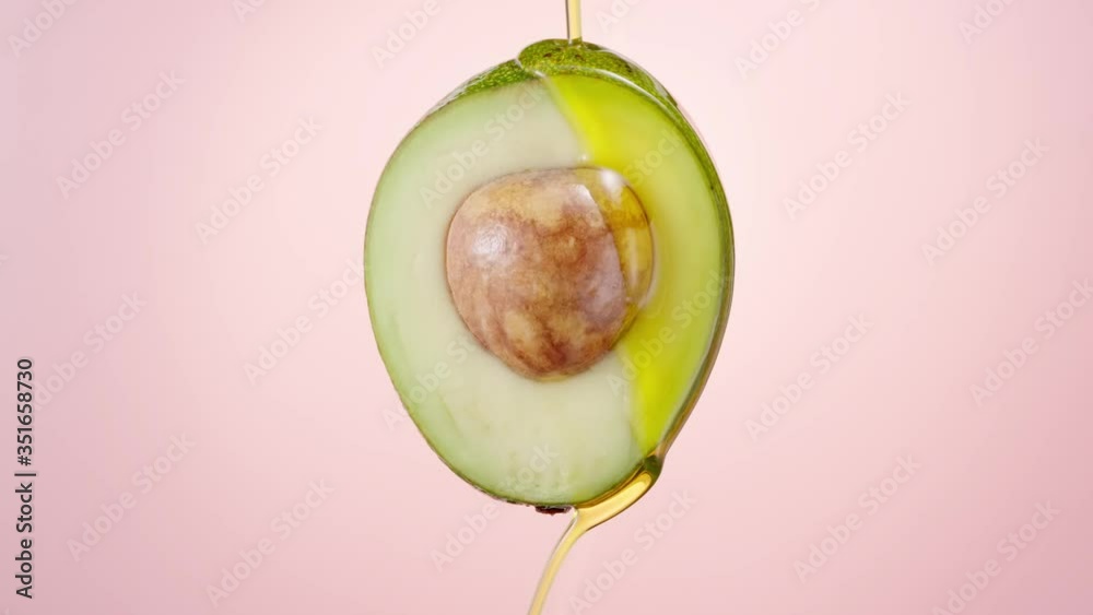 Fresh cut avocado covered with oil on nude pink background. Avocado oil pouring. Fresh cut avocado with oil stream. Slow motion, 4K 