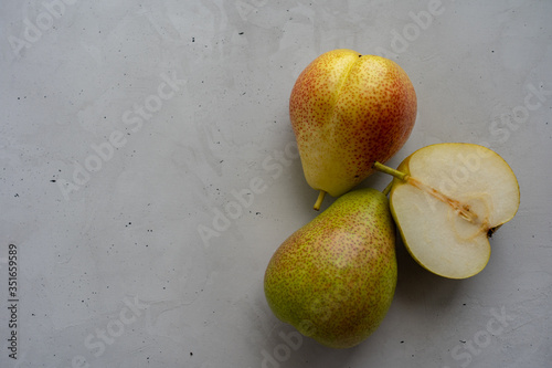 Two whole ripe pears and one half of a pear are laying at the right on concrete background