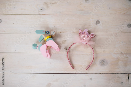 Little girls toys are on the wooden floor. 
A donkey figurine made of wood, as well as a pink head accessories 