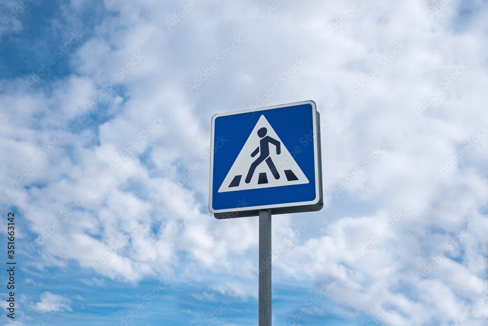 International traffic sign 'Pedestrian crossing'. Background contains cloudy blue sky