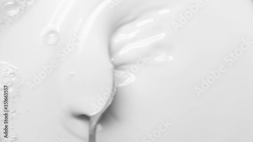 Fresh milk is mixed with a spoon. Closeup mixing white liquid with a spoon in Slow motion. Fresh soy milk in a transparent glass bowl. 