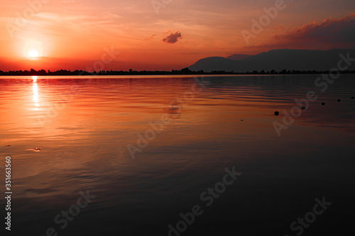 Cinematic red sunset sky reflected on the still waters of the Mekong River during the hot and humid summer season in Cambodia