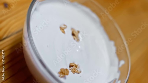 Granola fall into yogurt in a glass plate on a wooden table. Healthy breakfast or snacks, clean food concept. Slow motion