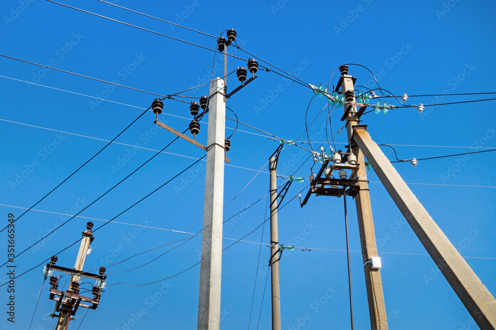 Multiple pillars of power line standing together close to each other. Clear blue sky is on background. View directed from bottom to up Multiple pillars of power line standing together close to each other. Clear blue sky is on background. View directed from bottom to up