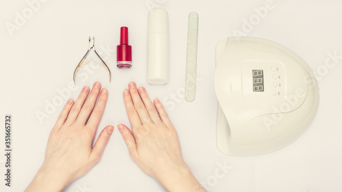Manicure and nail Polish concept. Uv-lamp, nail clipper, woman's hands, closeup, white background, top view, 16:9