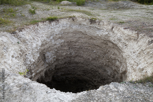 Black aperture of karst sinkhole, formed above abandoned limestone mine. Diameter about 15 ft, depth about 40-50 ft. Forming process is still going on